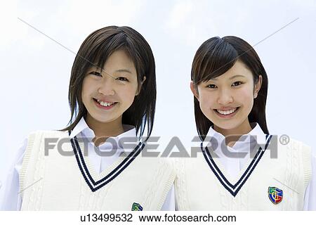 Stock Image - Portrait of teenage girls smiling and looking at camera under the blue sky, front view, Japan. Fotosearch