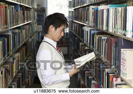 Stock Photography - Teenage boy reading a book in front of bookcase, side view. Fotosearch