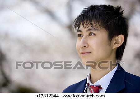 Picture - Teenage boy standing under cherry trees, looking away, side view, Japan. Fotosearch