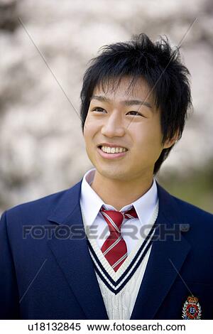 Stock Photography - Teenage boy standing under cherry trees, smiling, front view, Japan. Fotosearch