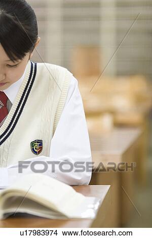 Picture - Teenage girl reading a book at table in library, front view. Fotosearch
