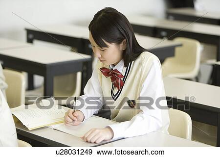 Stock Photo - Teenage girl sitting at desk and looking at text book in class, side view. Fotosearch