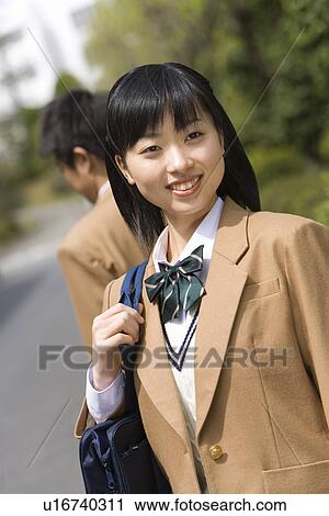 Stock Image - Teenage girl smiling and standing on the road, boy in background, front view, rear view, Japan. Fotosearch