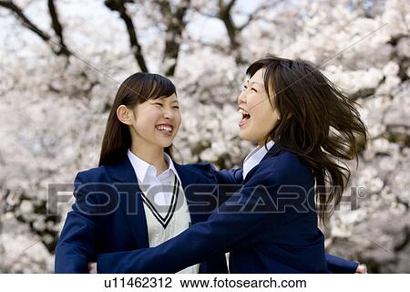 Stock Image - Teenage girls jumping and smiling under cherry trees, front view, side view, Japan. Fotosearch