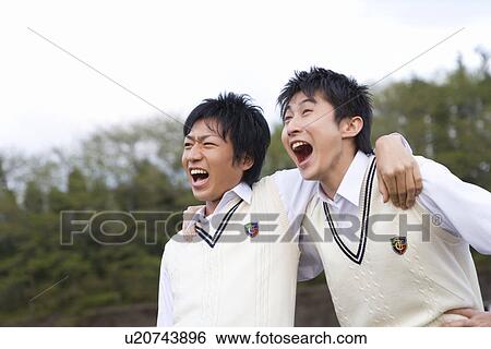 Stock Photograph - Two teenage boys putting arms around each other and yelling, front view, Japan. Fotosearch