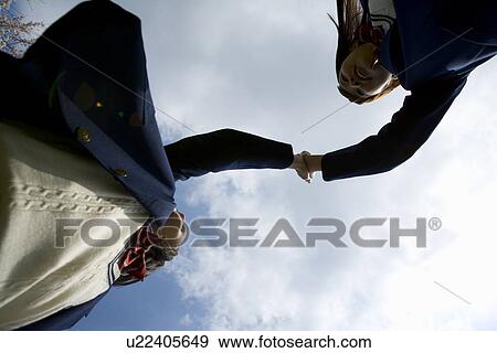 Stock Photo - Two teenage girls giving high fives, low angle view, Japan. Fotosearch