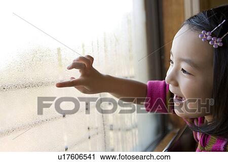 Stock Image - Girl drawing on window, smiling. Fotosearch