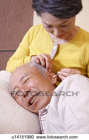 Stock Image - Senior woman cleaning senior man's ear. Fotosearch