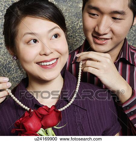 Stock Image - Close-up of a young man tying a necklace around a young woman's neck. Fotosearch