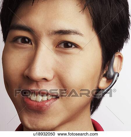 Stock Image - Portrait of a young man wearing a hands-free device. Fotosearch
