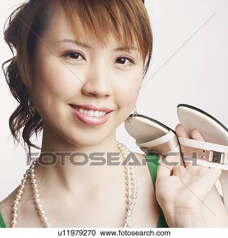 Stock Image - Portrait of a young woman holding a pair of slipper and smiling. Fotosearch