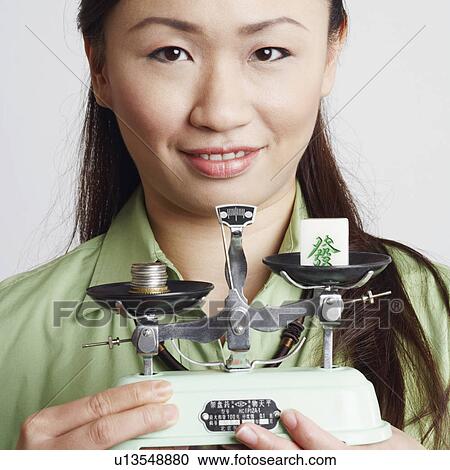 Stock Image - Portrait of a young woman holding a weighing scale and smiling. Fotosearch