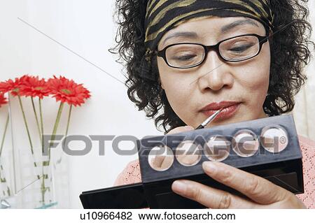Stock Image - Close-up of a mature woman applying lipstick on her lips. Fotosearch