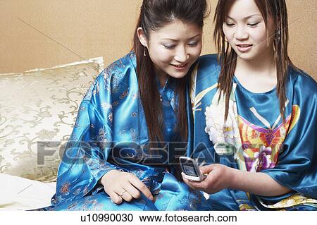 Close-up of a young woman sitting with a teenage girl looking at a mobile phone View Large Photo Image Stock Image - Close-up of a young woman sitting with a teenage girl looking at a mobile phone. Fotosearch