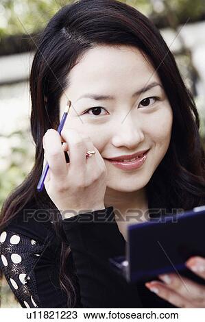 Stock Image - Portrait of a young woman applying eyeshadow smiling. Fotosearch