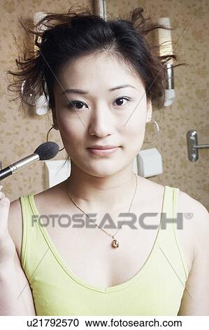 Portrait of a young woman applying make-up on her face View Large Photo Image Stock Image - Portrait of a young woman applying make-up on her face. Fotosearch