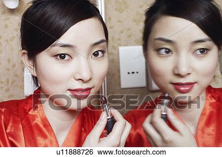 Portrait of a young woman applying lipstick View Large Photo Image Stock Photograph - Portrait of a young woman applying lipstick. Fotosearch