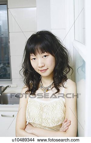 Picture - Portrait of a young woman standing in the kitchen with her arms folded. Fotosearch