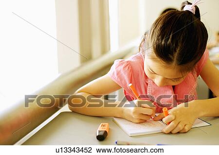 Stock Image - Close-up of a girl writing on a spiral notebook in the classroom. Fotosearch