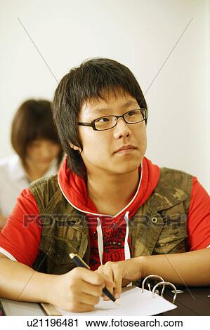 Stock Image - Close-up of a teenage boy holding a pen on a spiral notebook. Fotosearch