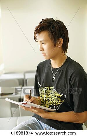 Picture - Close-up of a teenage boy writing on a notepad and sitting in the classroom. Fotosearch