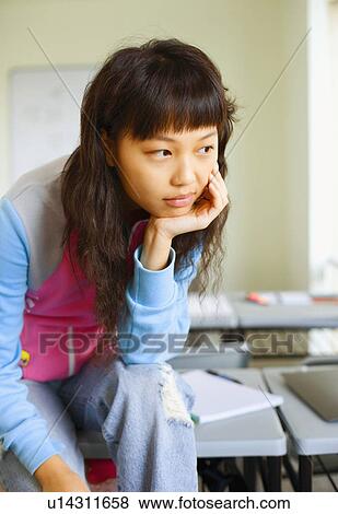 Close-up of a young woman sitting on desk and thinking in the classroom View Large Photo Image Stock Photo - Close-up of a young woman sitting on desk and thinking in the classroom. Fotosearch