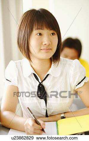 Stock Photo - Close-up of a young woman writing on a notepad in a classroom. Fotosearch