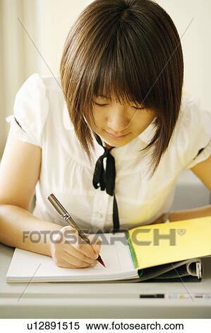 Stock Photography - Close-up of a young woman writing on a notepad in a classroom. Fotosearch