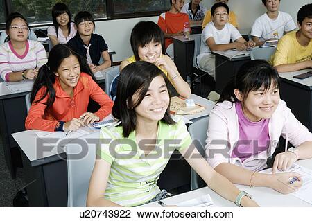 Stock Image - Group of teenage boys and teenage girls sitting in a classroom and smiling. Fotosearch