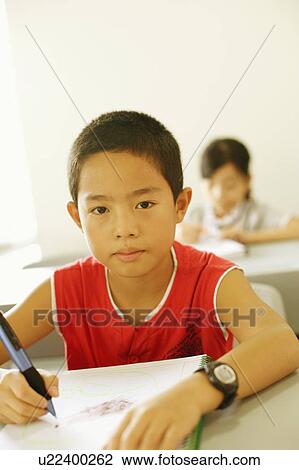Stock Image - Portrait of a boy writing on a spiral notebook in the classroom. Fotosearch