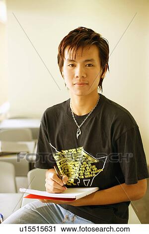 Stock Image - Portrait of a teenage boy holding a pen on a notepad in a classroom. Fotosearch