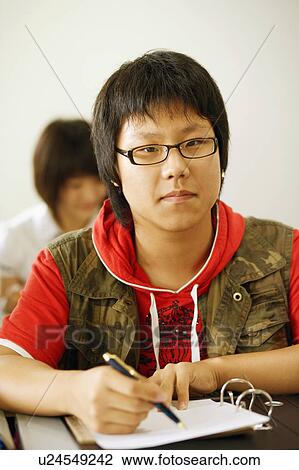 Stock Image - Portrait of a teenage boy holding a pen on a spiral notebook. Fotosearch