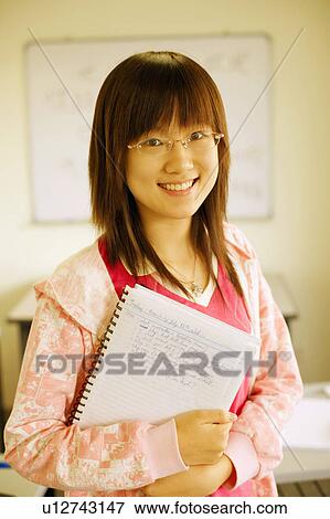 Stock Photo - Portrait of a teenage girl holding a spiral notebook and smiling in the classroom. Fotosearch