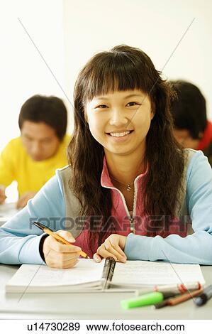 Stock Photo - Portrait of a young woman sitting at a desk in the classroom and smiling. Fotosearch