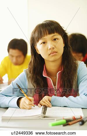 Stock Photograph - Portrait of a young woman sitting at a desk in the classroom. Fotosearch