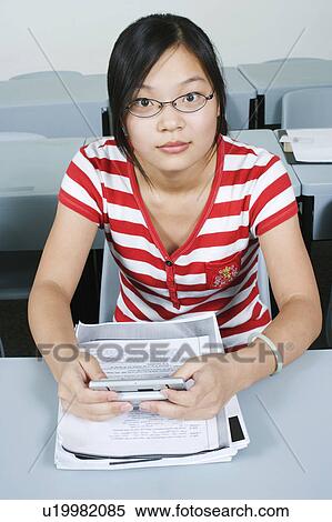 Stock Photography - Portrait of a young woman sitting in the classroom and holding a personal data assistant. Fotosearch