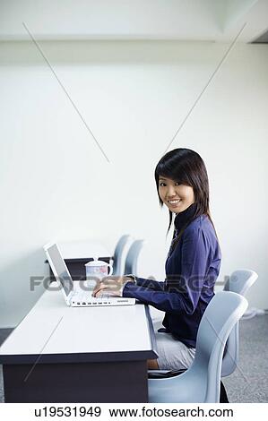 Portrait of a young woman smiling and using a laptop View Large Photo Image Stock Photo - Portrait of a young woman smiling and using a laptop. Fotosearch