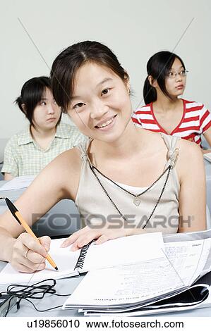 Portrait of a young woman writing in the classroom and smiling View Large Photo Image Stock Image - Portrait of a young woman writing in the classroom and smiling. Fotosearch