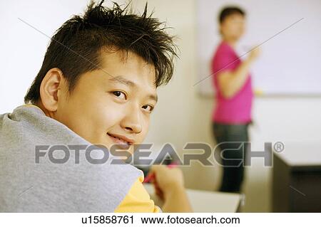 Stock Image - Rear view of a young man sitting in a classroom and smiling. Fotosearch
