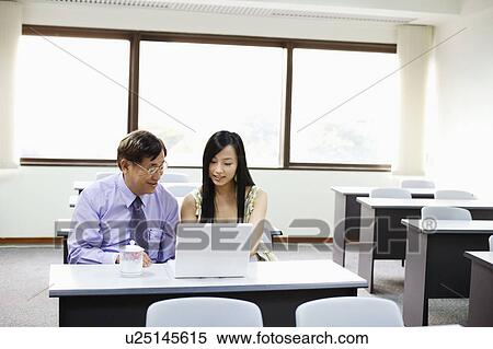 Stock Photography - Senior man and a young woman using a laptop in a classroom. Fotosearch