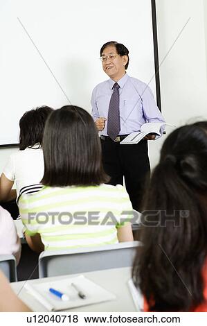 Teacher teaching in a classroom and smiling View Large Photo Image Stock Photo - Teacher teaching in a classroom and smiling. Fotosearch