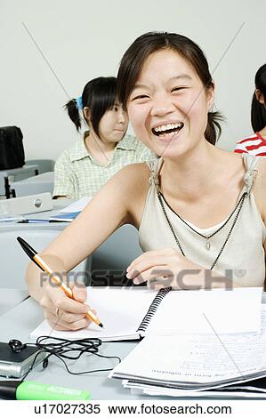 Stock Photography - Young woman writing in a classroom and smiling. Fotosearch