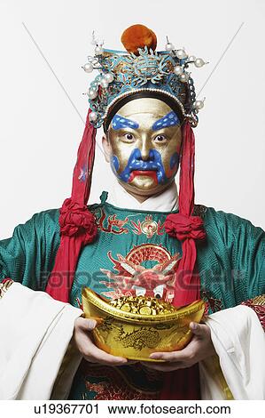 Stock Image - Portrait of a male Chinese opera performer holding a bowl full of gold coins. Fotosearch