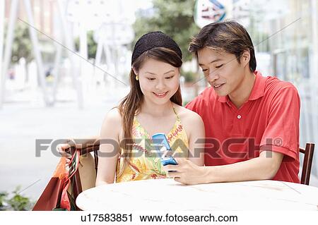 Close-up of a young couple sitting in a cafeteria and looking at mobile phone View Large Photo Image Stock Image - Close-up of a young couple sitting in a cafeteria and looking at mobile phone. Fotosearch