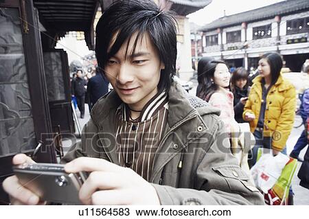 Stock Image - Close-up of a young man holding a camera smiling. Fotosearch
