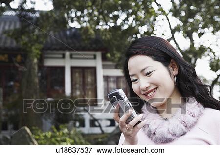 Stock Photo - Close-up of a young woman looking at a mobile phone smiling. Fotosearch