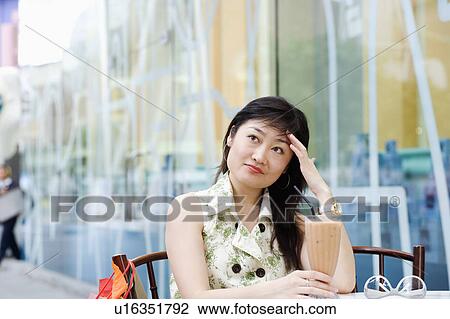 Stock Image - Close-up of a young woman sitting in a cafeteria with her hands on her head. Fotosearch