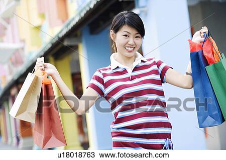 Stock Image - Portrait of a young woman holding shopping bags and smiling. Fotosearch