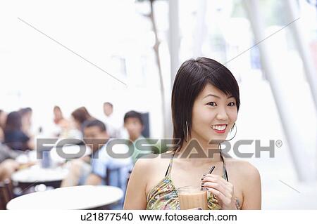 Stock Image - Young woman holding a glass of milkshake. Fotosearch