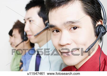 Stock Image - Four customer service representatives talking on headsets. Fotosearch